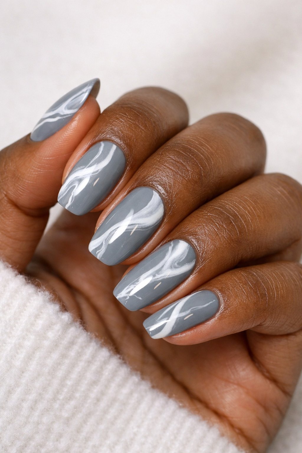 Close-up of a dark-skinned hand with gray and white marbled nail art on winter-themed nails.