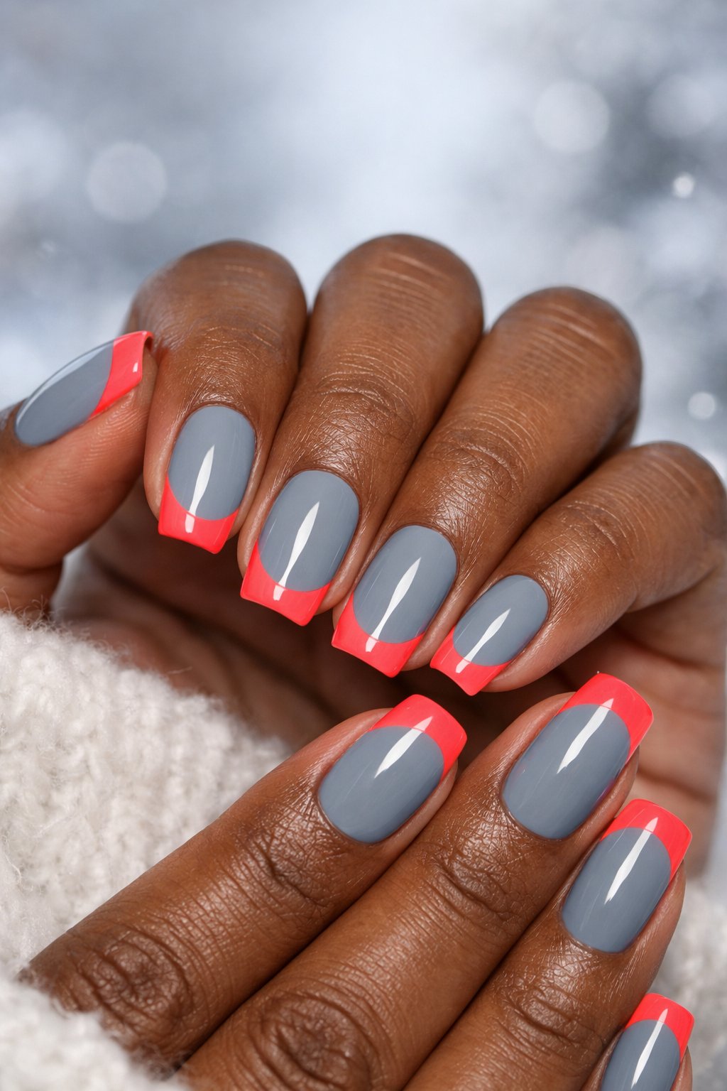 Close-up of a woman's dark skin hands with gray nails and bright coral tips.