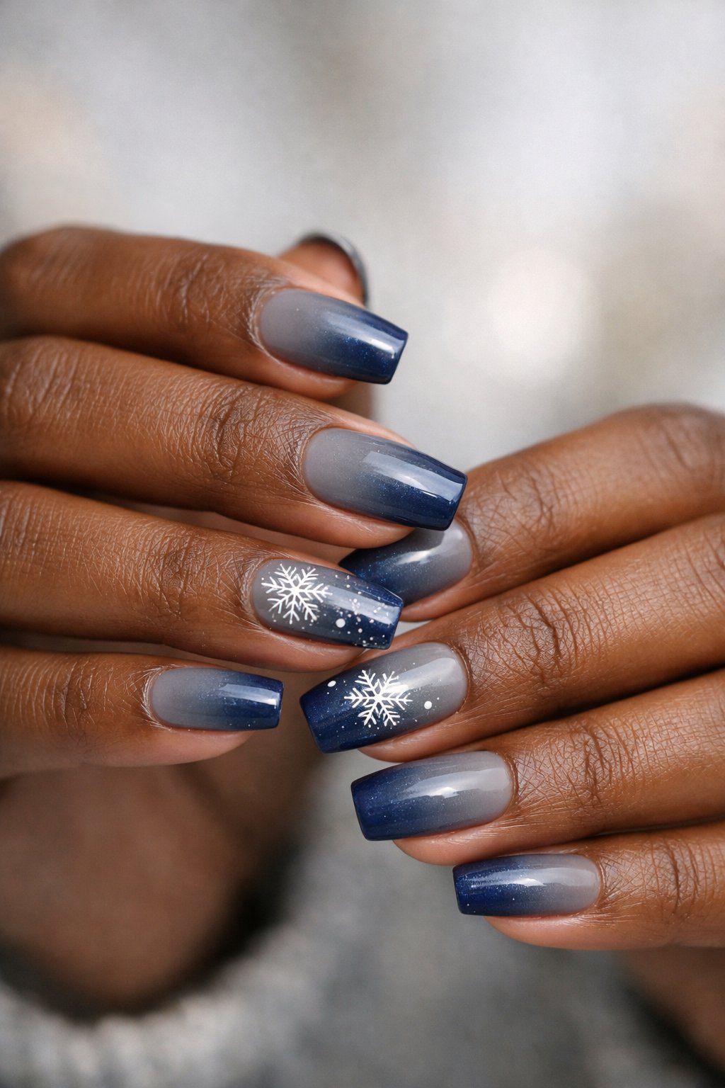 Close-up of dark-skinned hands showing nails painted in gray and deep blue gradient colors.