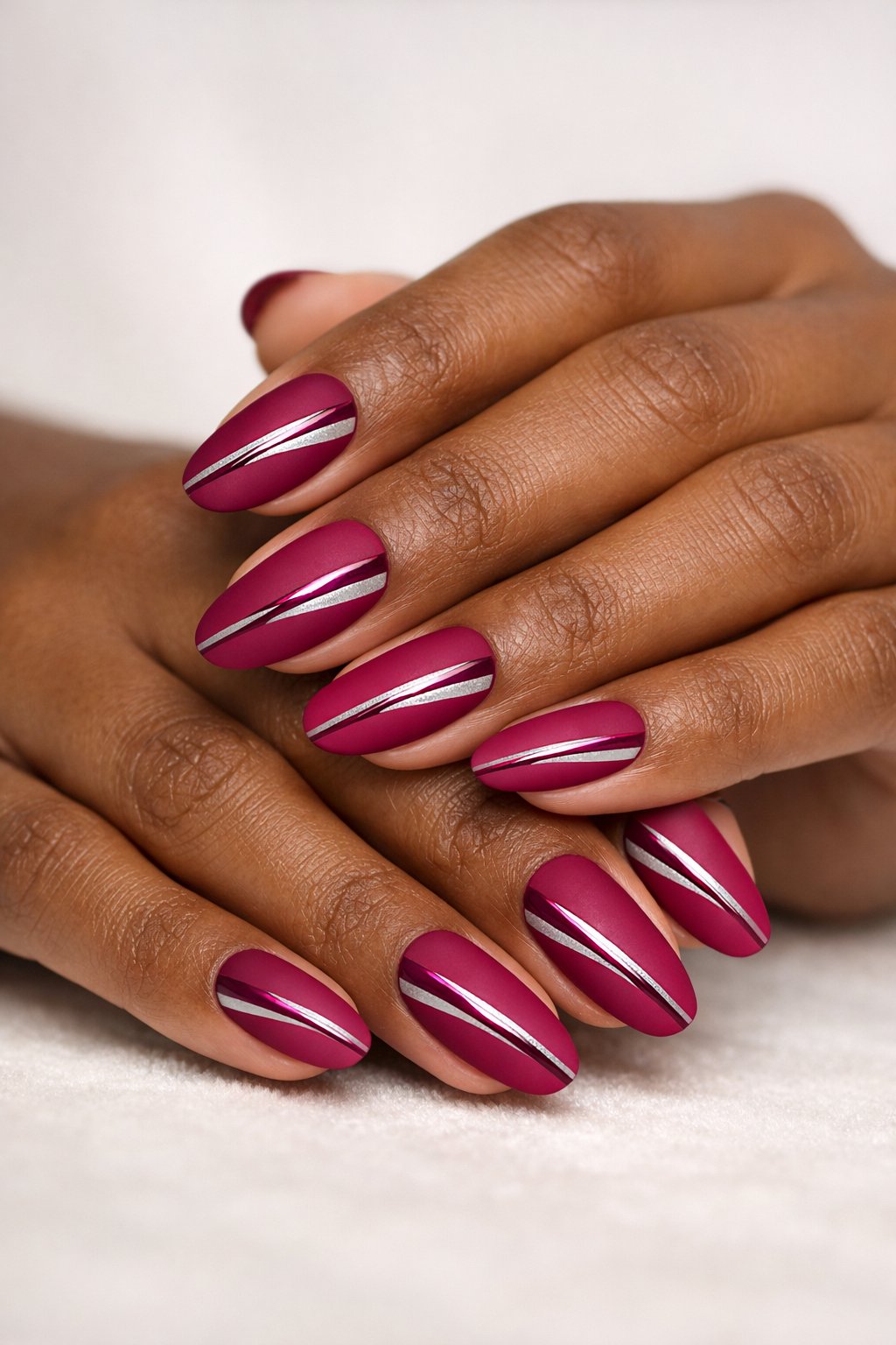 Close-up of dark-skinned hands with magenta matte nails featuring glossy stripes.