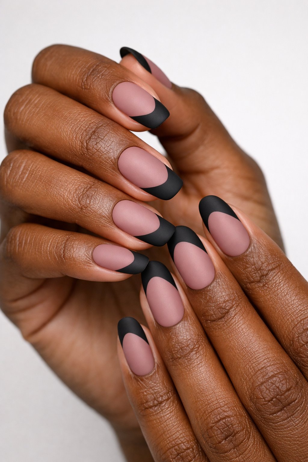 Close-up of dark-skinned hands with nails painted dusty rose and matte black tips.