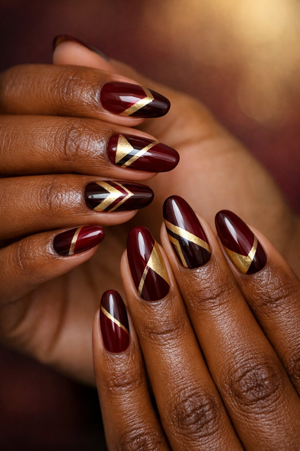 Close-up of hands with maroon and gold geometric patterned nails on dark skin tone.