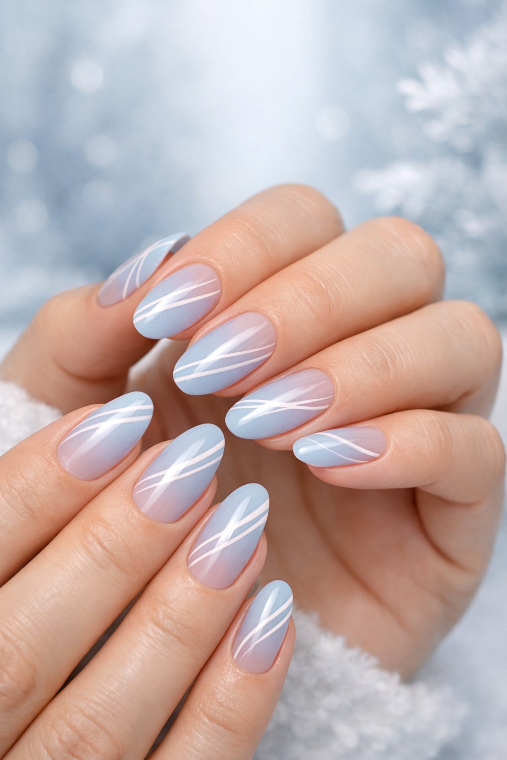 Close-up of hands with blue nails featuring white stripes on a soft winter-colored background.