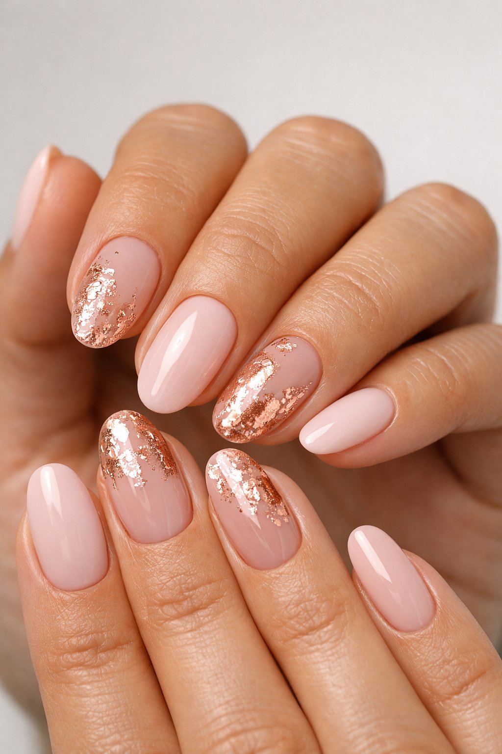 Close-up of manicured hands with nails featuring rose gold foil accents on nude and pale pink bases.