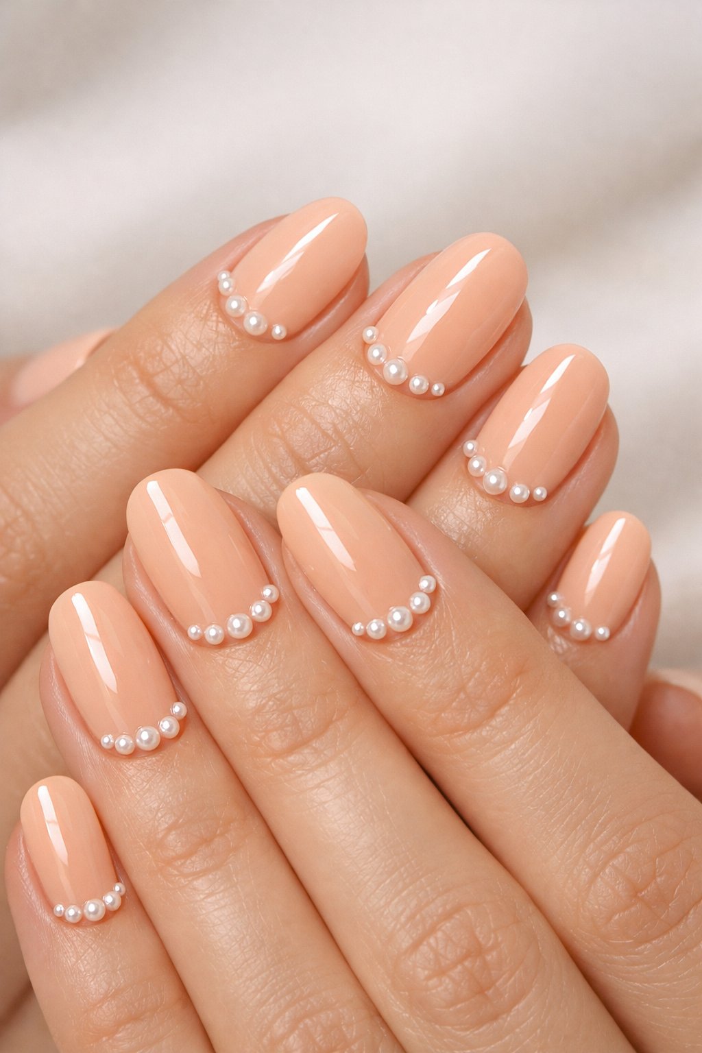 Close-up of hands with pale peach glossy nails decorated with small pearl studs.