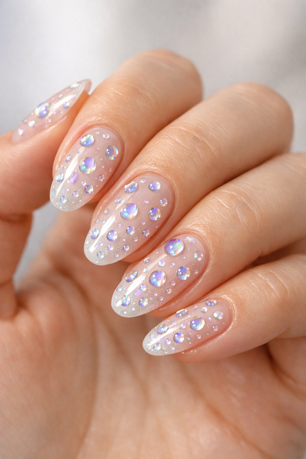 Close-up of a woman's hand displaying nails with holographic raindrop designs on a soft blurred background.