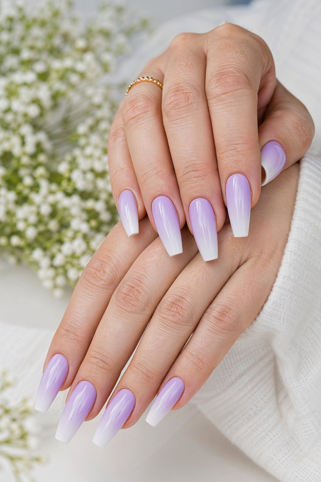 Close-up of hands with lilac ombré coffin-shaped nails against a soft background with blurred spring flowers.