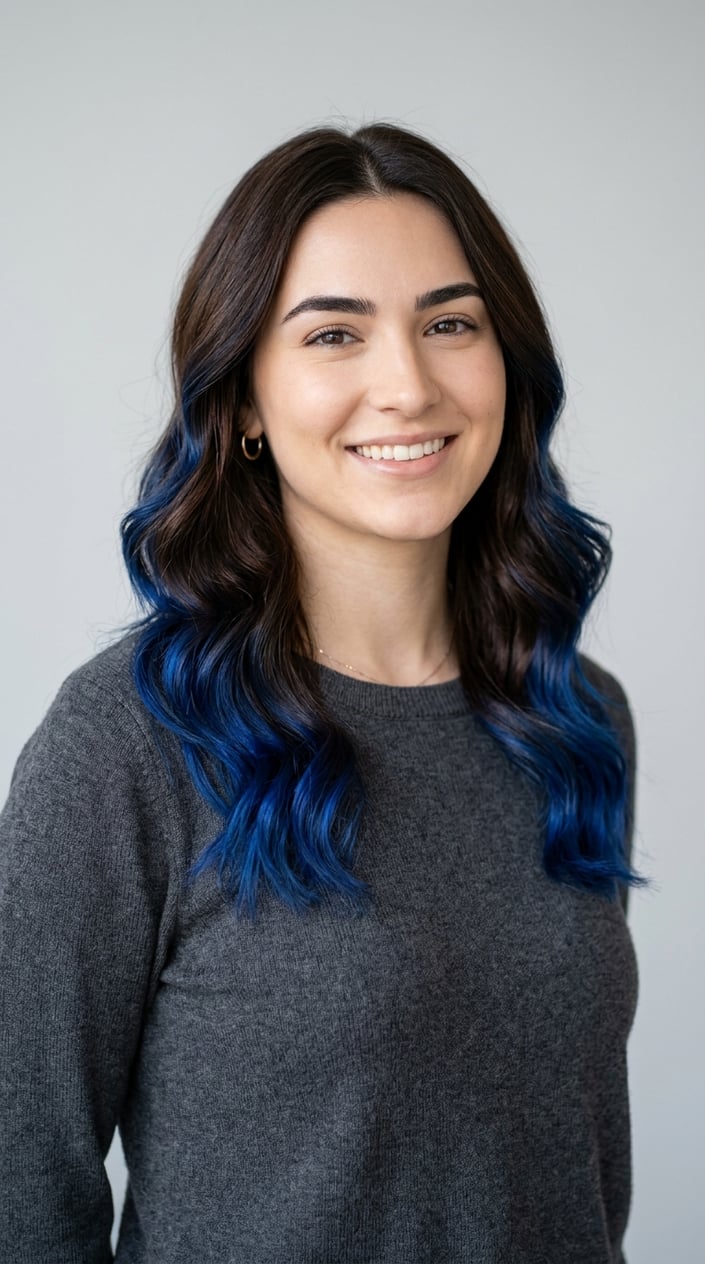 A young woman with espresso brown hair and sapphire blue tips styled in soft waves against a neutral background.