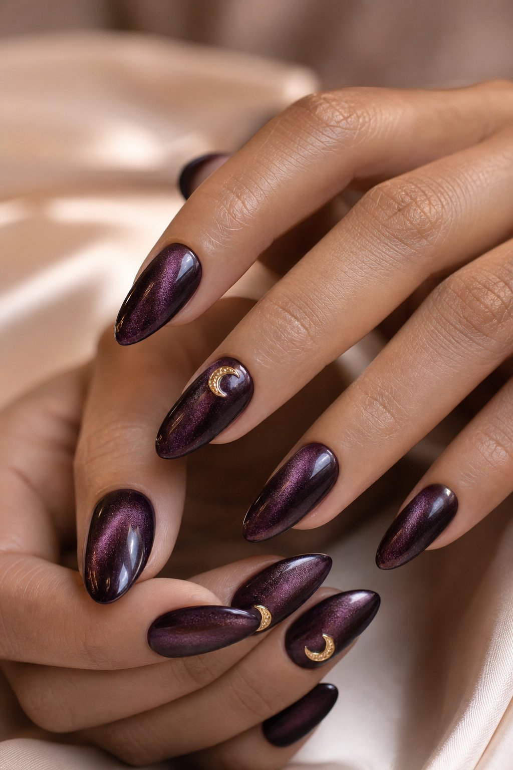 Hands with deep plum velvet-finish nails decorated with small gold crescent-moon charms.