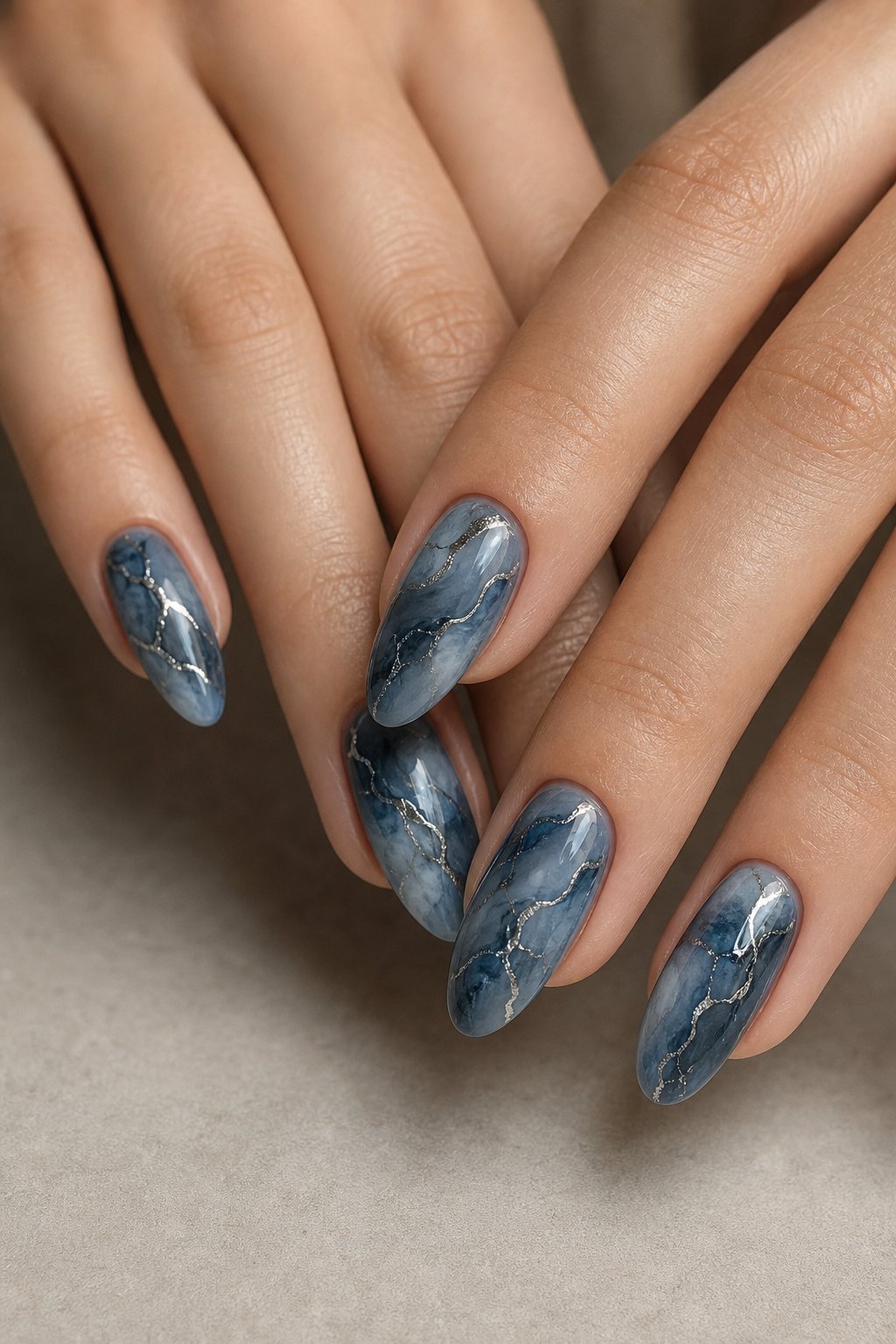 A close-up of hands with smoky blue marble-patterned nails featuring silver veins.