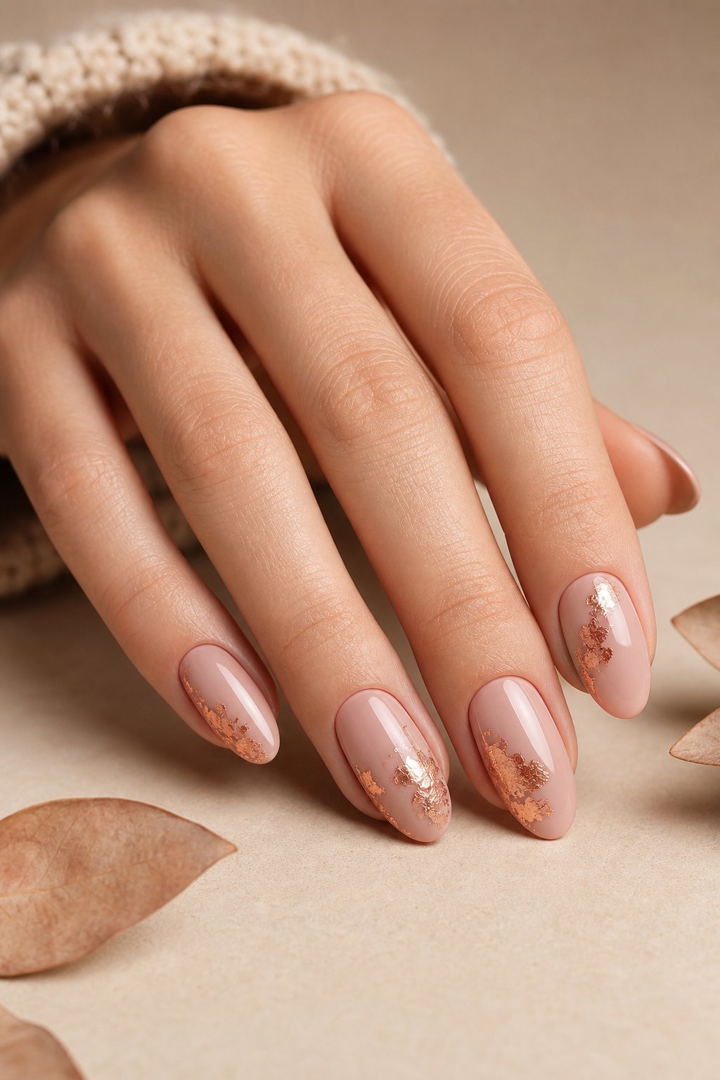 A hand with nude pink almond-shaped nails decorated with delicate copper foil accents.