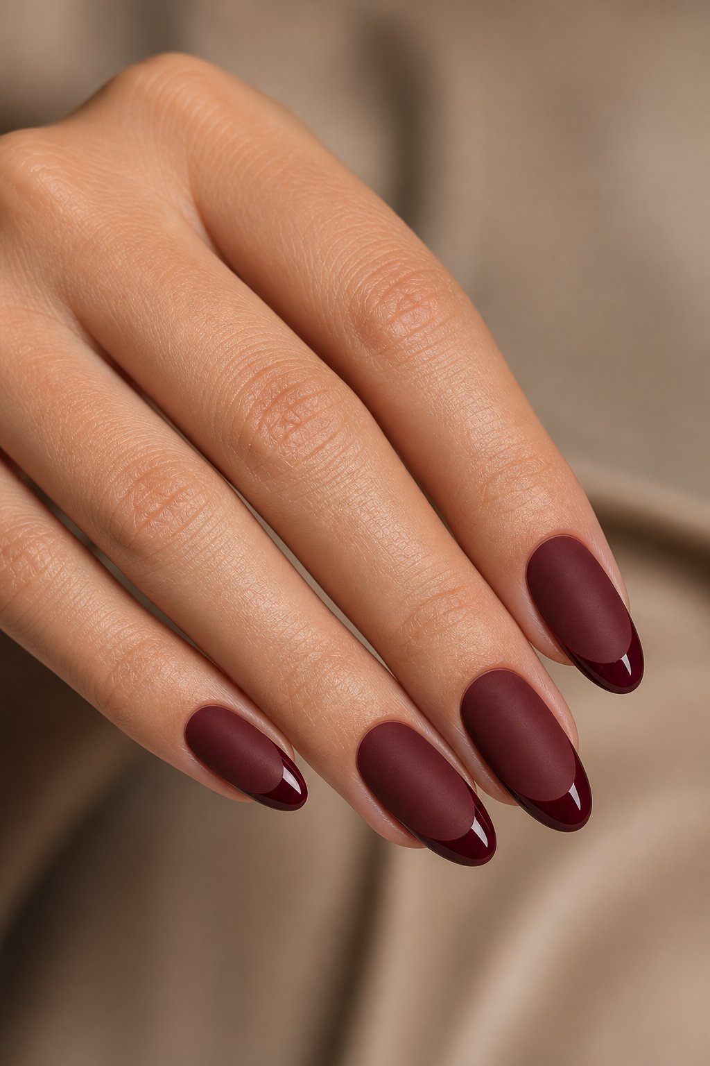 A hand with matte wine-red almond-shaped nails and glossy wine-red tips.